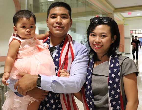 Young parents holding an infant, with United States flags draped over their shoulders