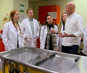 Students in lab coats standing in hopsital setting with instructor. 