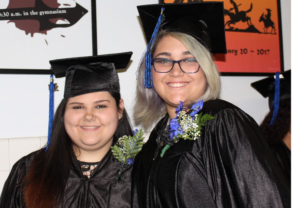 Two smiling students in black caps and gowns pose for photos before the Maywood School graduation.
