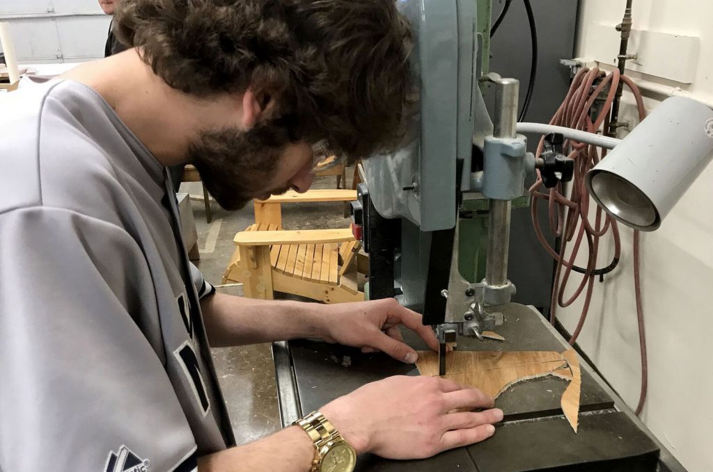 Student with head bent cuts a piece of wood with electric jigsaw.