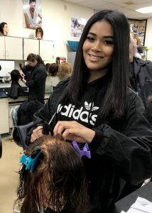 Cosmetology graduate Zoey Lukasik smiles as she practices hair techniques in the classroom.