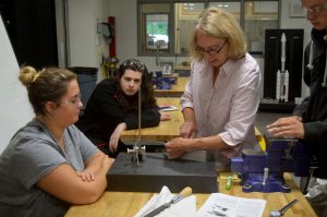 Students and a teacher gather around a machine used to make precise measurements needed when making metal parts.