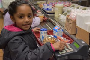 Elementary-age girl with a full lunch tray stops to pay for her meal at a self-serve keypad.