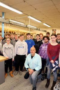 A group of students are pictured with their teacher in the electrical trades classroom
