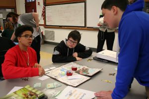 Three middle school-age boys gather around a board game they designed as part of a class project on evolution.