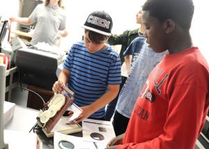 Two students, one wearing a baseball cap, the other in a red sweatshirt, work together on a project during the BOCES Career and Technical School Summer Camp. 
