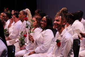 Seated on the stage of Proctors Theatre, CTE Adult Nursing students, dressed in white uniforms and holding red roses, smile during at their June 26 graduation ceremony.