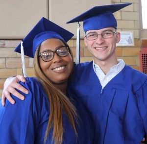 Two adult education graduates dressed in bright blue caps and gowns smile for the camera