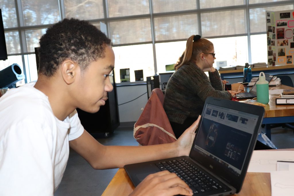 A seated student in a coding class looks at a laptop screen.