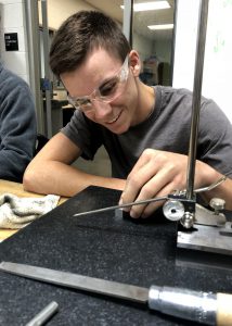 A male student, wearing protective eye wear, works at a macine in a Capital Region BOCES Machining and Manufacturing classroom.