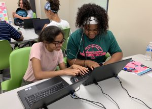 Two high school age girls work together at a laptop computer during a summer coding camp.