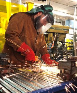 Sparks fly as Capital Region BOCES welding student Brendan Frank, dressed in protective clothing, works at a welding machine.
