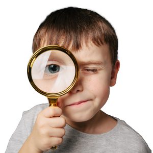 Young boy looks through the lens of an oversized magnifying glass.