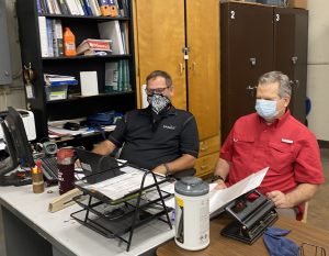 Two teachers wearing face coverings sit side by side watching a staff training on a computer.