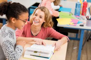 Adult kneels at student's desk helping with work