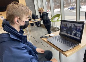 Capital Region BOCES Game Design and Implementation student, wearing a navy blue windbreaker and black protective face covering, attends a virtual meeting on a laptop computer with Vicarious Visions game designers.