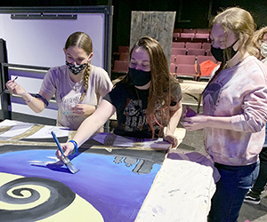 Three students in Capital Region BOCES Entertainment Technology program stand together as they paint scenery on a table on-stage at Proctors Theatre in Schenectady, NY.