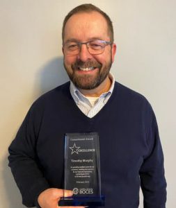 Capital Region BOCES Health, Safety, Risk program coordinator Tim Murphy, who has short hair, and is wearing a light green oxford shirt and eyeglasses, smiles for the camera.