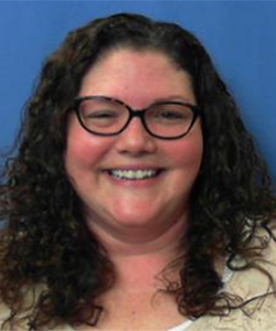 Capital Region BOCES Administrative Aide Linda Stapleton, who has long brown curly hair and is wearing a light yellow top and tortoise-framed eyeglasses, smiles for the camera. Linda is Capital Region BOCES' March 2021 commitment award recipient for improvement.