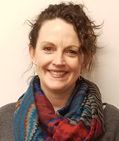 Albnay Campus Career & Technical School Assistant Principal Kathleen Nickerson, with brown hair pulled back away from their face and wearing a brown top and multicolored scarf, looks at and smiles for the camera.