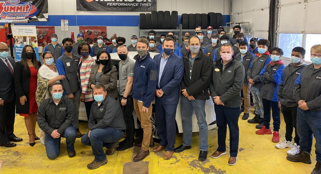 A group of adults and students gather for a group photograph in the automotive garages at the Career & Technical School.