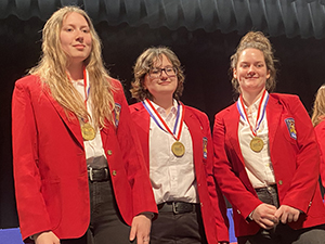 Criminal Justice students Breanna Powell, Chloe-Jean "CJ" Thomas and Erin Haugh stand shoulder to shoulder and pose for the camera after winning first place in the 2022 Regional Skills USA competion. All are wearing red SkillsUSA blazers, white shirts and black jeans.