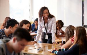 A teacher smiles over students working.