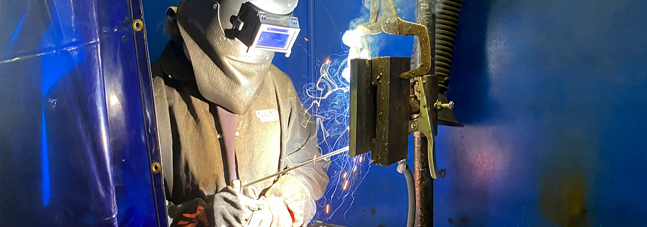 Welding students in protective clothing work together on a project. 