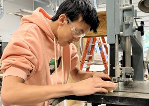 A building trades student holds a piece of wood under a machine..
