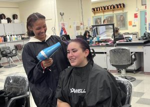 Cosmetology students Kristyna Butcher and Kloey Barber smile as one student blow dries the other's hair.