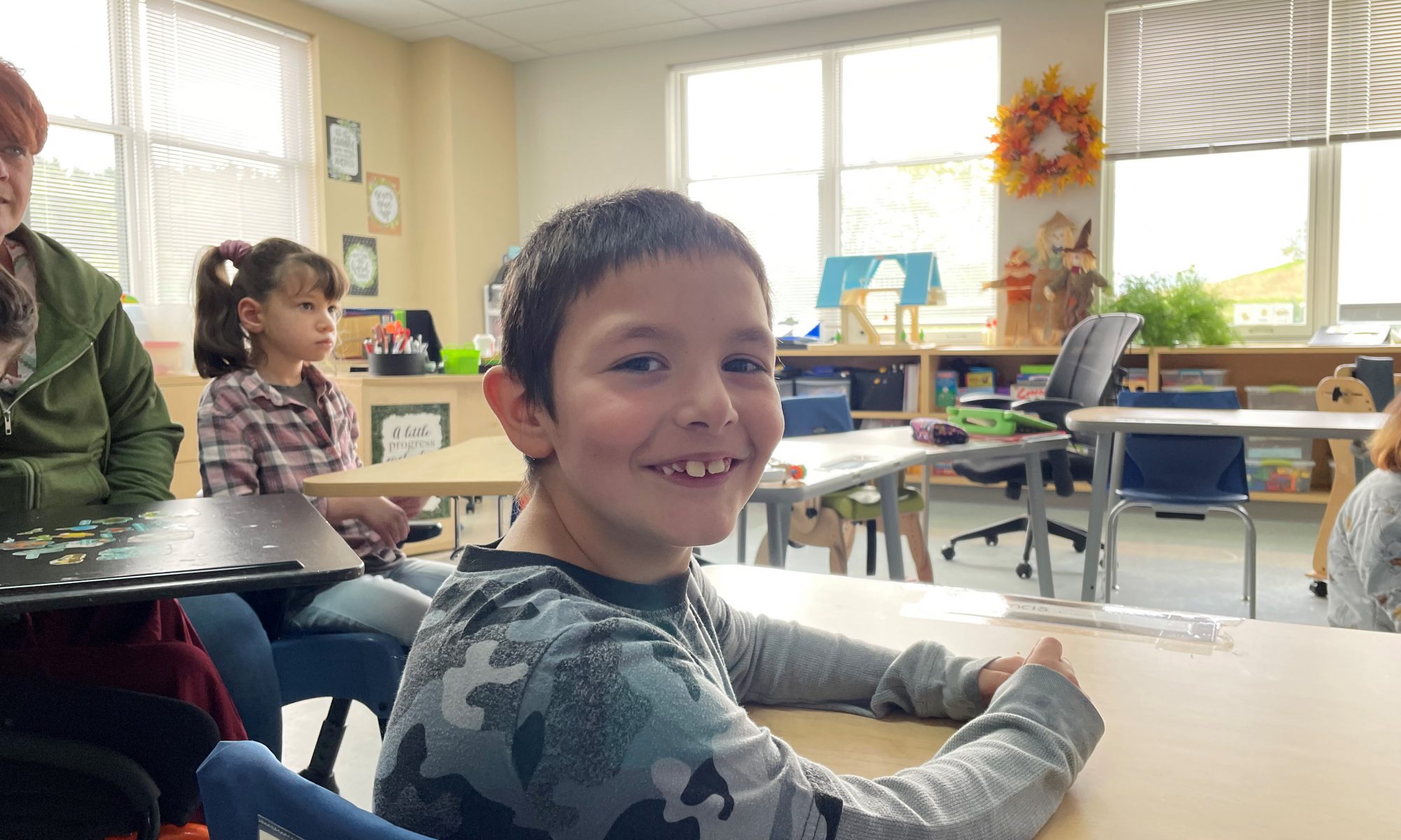 A student smiling, looking behind them. They are wearing a grey camo shirt.