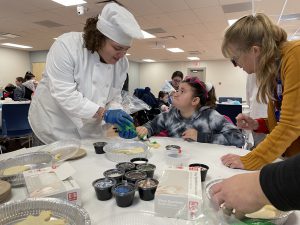 A culinary student helps a Maywood Academy student pipe frosting onto a cookie.