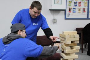 Two students in blue shirts playing with large Jenga blocks.