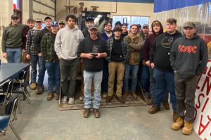 Matt Millard holds a crystal award. Behind them is a group of students.