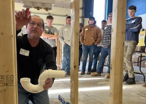 An individual holds PVC piping while students observe.