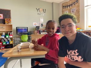 Two students sitting at a desk, looking at the camera smiling