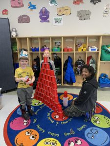Two students standing next to a tower of red plastic cups, one student kneeling next to the tower. All three individuals are smiling at the camera.