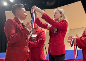 An individual with a red SkillsUSA jacket in the act of placing a medal around SkillsUSA student Gino Isabella