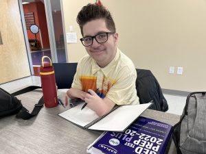 Student Dylan Quiros sitting at a desk, smiling with a notebook and pen.