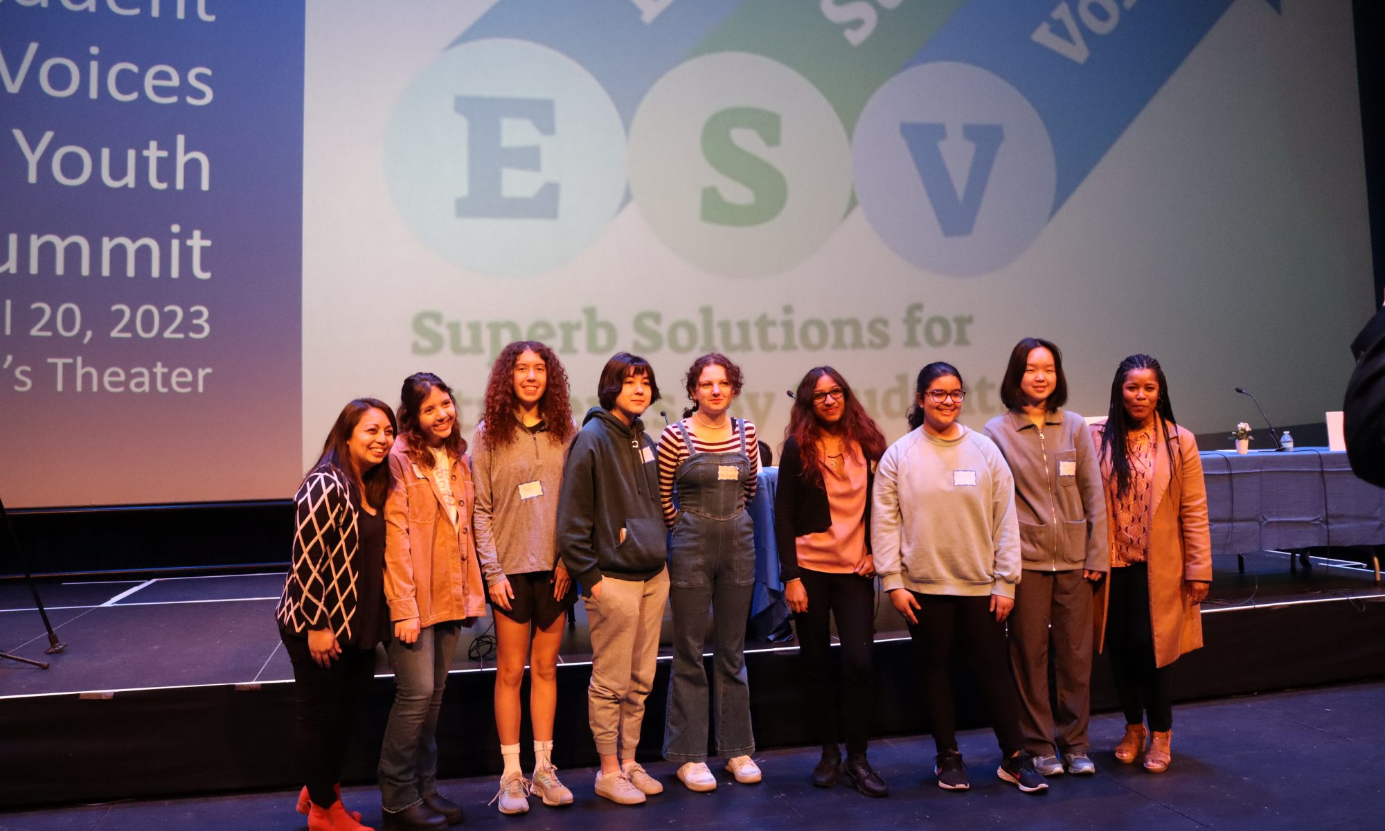 A group of nine students standing next to each other on stage, smiling at the camera.