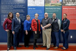 Group photo of Commissioner Reardon, Dr. Joseph Dragone and five individuals smile in front of a mural.