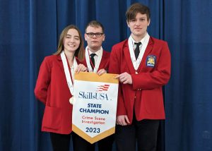 Three students in SkillsUSA red coats hold a SkillsUSA state champions banner.
