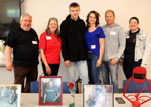 Capital Region BOCES student Clay Smith, who has short light brown hair and is wearing a black buttoned shirt and jeans, stands in the center of a row of people who are looking at and smiling for the camera. 