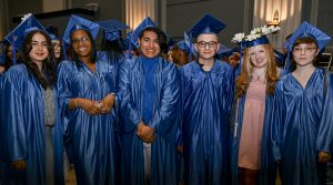 Six students in blue graduation regalia smile at the camera.
