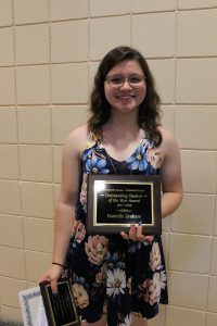 A graduate stands holding a plaque.