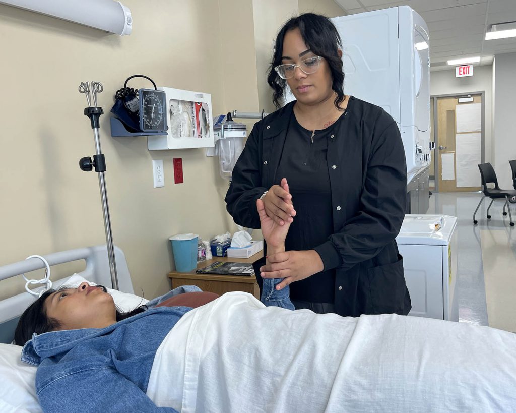 one student takes the pulse of another student lying in bed