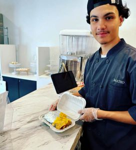 A young man shows off a container of food sitting on top of a counter top.