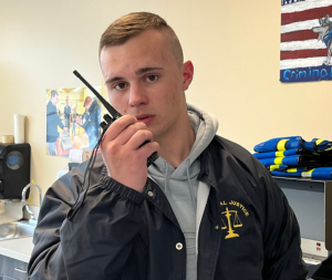 A criminal justice student in a blue jacket looks into the camera as he speaks into a handheld radio.