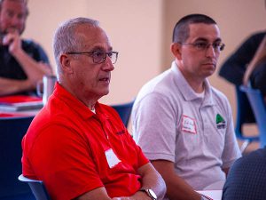 Two men, one in a red shirt and another in an off white shirt, speak at a roundtable discussion hosted by Capital Region BOCES.