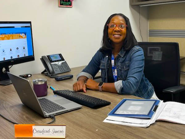 The new program principal sits behind her desk with her name tag reading Lessa Crawford-Imoro in the foreground.